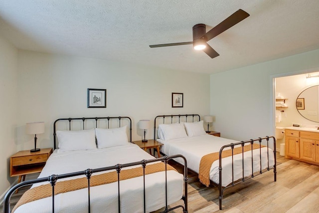 bedroom featuring light wood-type flooring, ensuite bath, a ceiling fan, and a textured ceiling