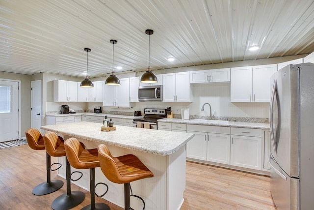 kitchen with a sink, light wood-style floors, a kitchen breakfast bar, appliances with stainless steel finishes, and a center island