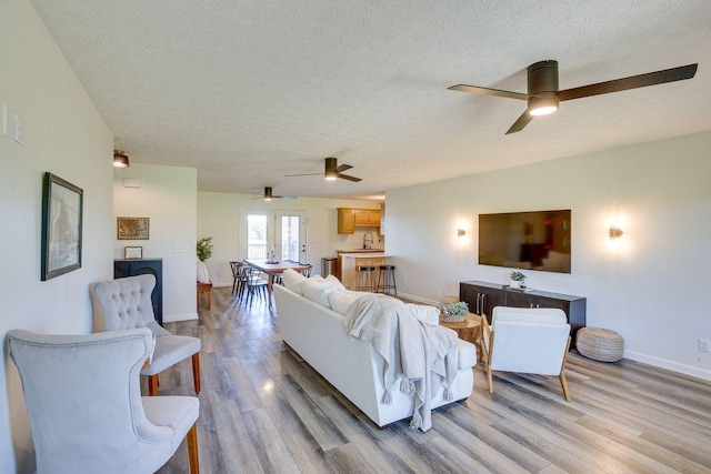 living area with baseboards, light wood-style flooring, and a textured ceiling