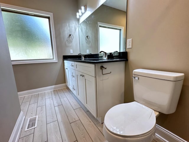 bathroom with visible vents, toilet, vanity, wood finished floors, and baseboards