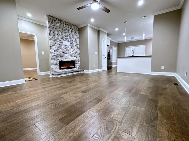 unfurnished living room with ceiling fan, a stone fireplace, dark wood-style flooring, and baseboards