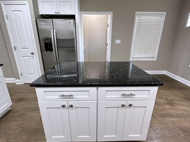 kitchen featuring baseboards, dark stone counters, white cabinets, stainless steel fridge with ice dispenser, and a kitchen island