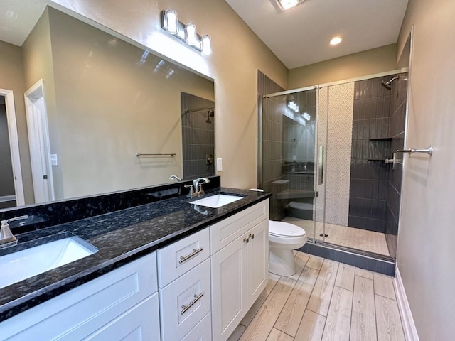 bathroom with toilet, a stall shower, a sink, and wood finished floors