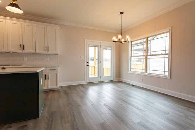 unfurnished dining area featuring baseboards, an inviting chandelier, wood finished floors, and crown molding