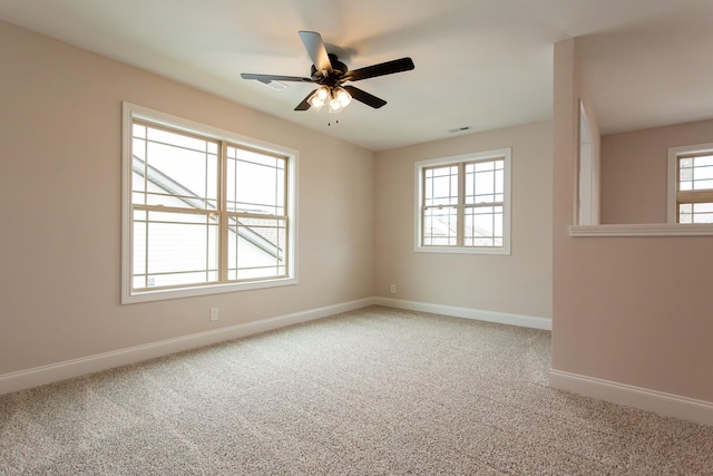 carpeted spare room with visible vents, baseboards, and ceiling fan