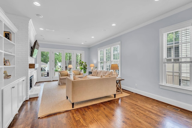 living area featuring baseboards, visible vents, ornamental molding, wood finished floors, and a fireplace