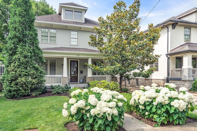 american foursquare style home with covered porch, roof with shingles, and a front lawn