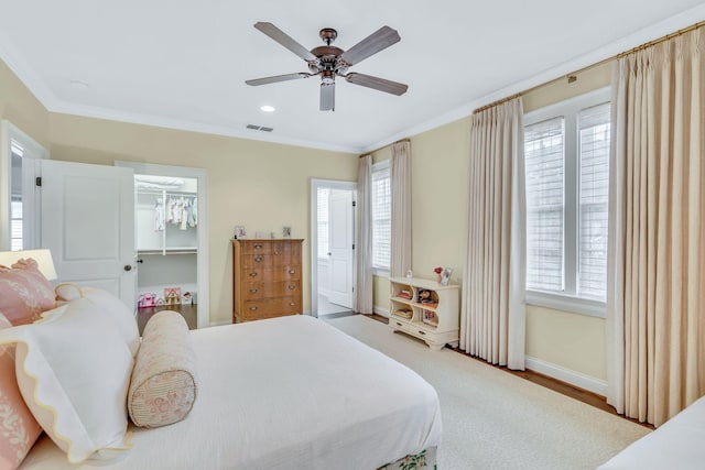 bedroom with a walk in closet, visible vents, crown molding, and baseboards