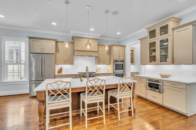 kitchen featuring appliances with stainless steel finishes, light wood-style floors, a center island with sink, and a kitchen bar