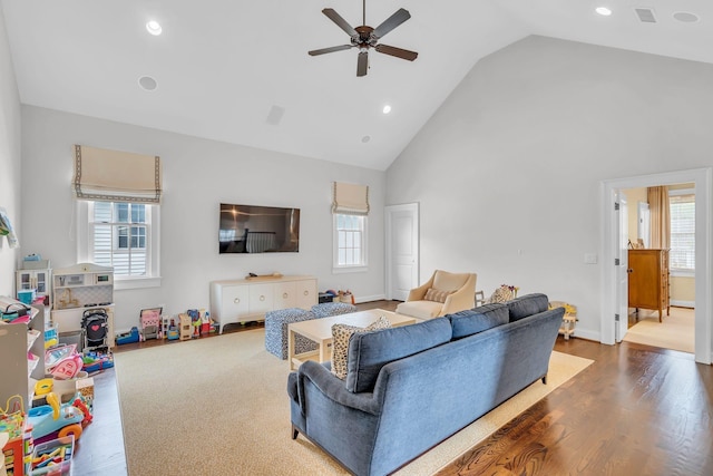 living area with high vaulted ceiling, a wealth of natural light, ceiling fan, and wood finished floors