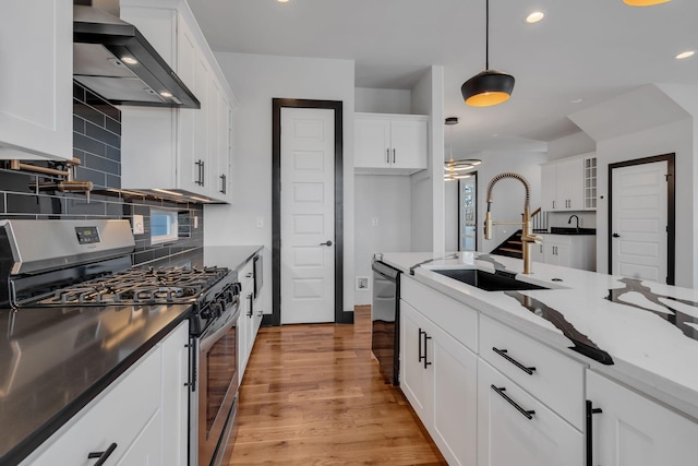 kitchen with stainless steel range with gas cooktop, light wood finished floors, white cabinets, a sink, and wall chimney range hood