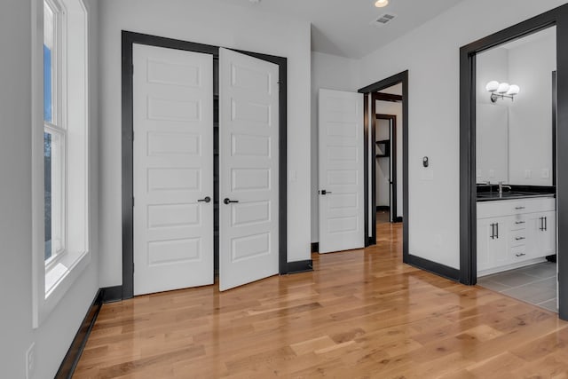 unfurnished bedroom with visible vents, a sink, light wood-style flooring, and baseboards