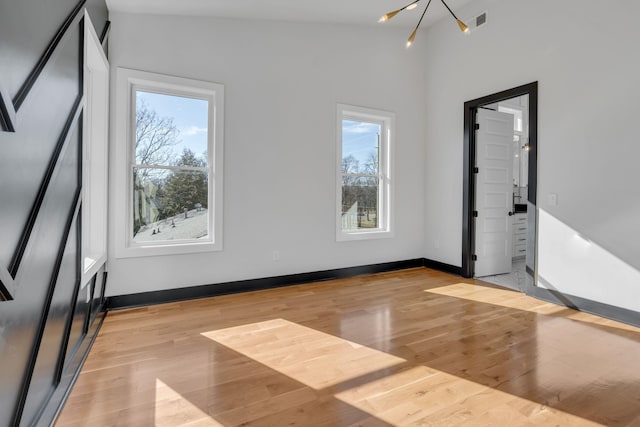 empty room featuring light wood-style floors, visible vents, baseboards, and an inviting chandelier