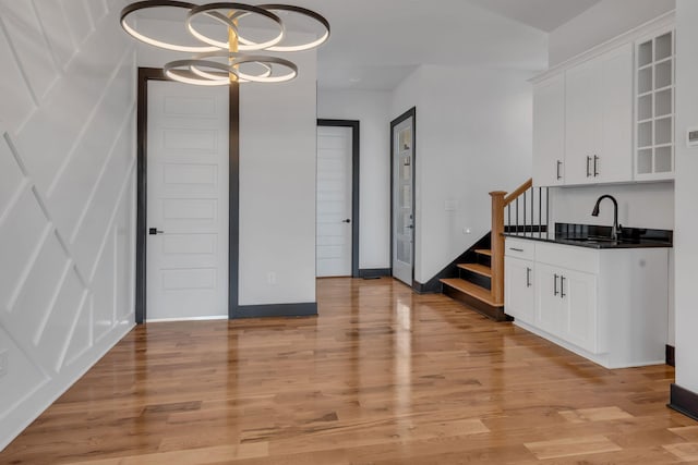 unfurnished dining area with baseboards, light wood-style flooring, stairway, a chandelier, and a sink