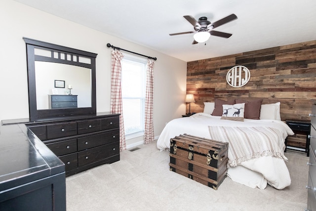 bedroom featuring visible vents, ceiling fan, an accent wall, carpet, and wood walls