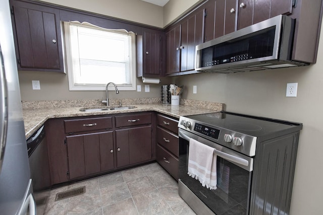 kitchen featuring visible vents, light stone countertops, stainless steel appliances, dark brown cabinets, and a sink