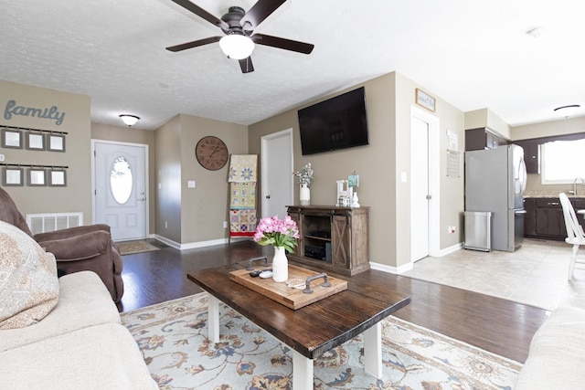 living room featuring light wood-style floors, baseboards, visible vents, and a textured ceiling