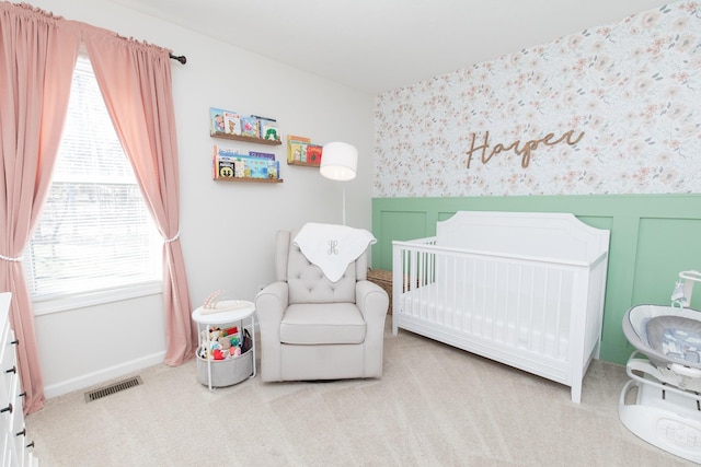 bedroom with a decorative wall, a wainscoted wall, carpet floors, visible vents, and a crib