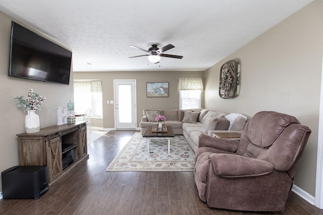 living room with ceiling fan, a textured ceiling, baseboards, and dark wood-type flooring