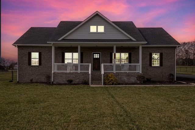 view of front of property featuring covered porch, a yard, brick siding, and a shingled roof