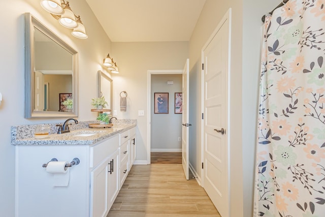 bathroom with double vanity, baseboards, a sink, and wood finished floors