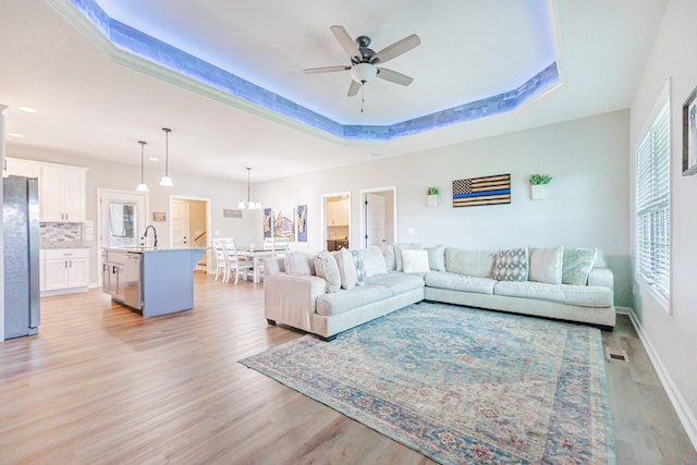 living area featuring visible vents, baseboards, light wood-style flooring, ceiling fan, and a tray ceiling