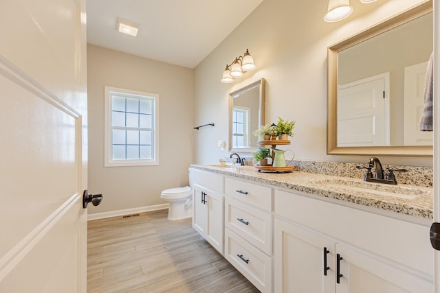 full bathroom with toilet, double vanity, a sink, and wood finished floors