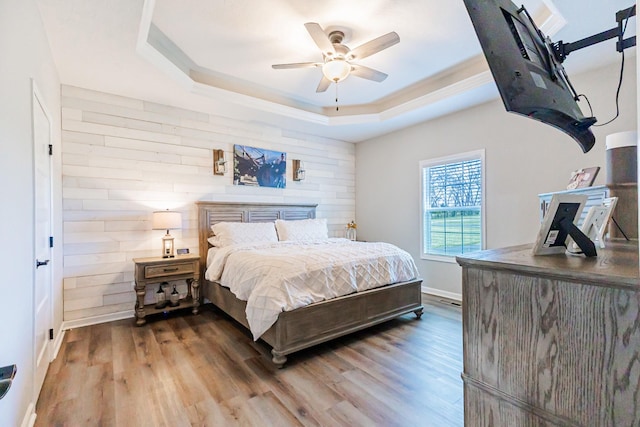 bedroom with ceiling fan, baseboards, a raised ceiling, and wood finished floors