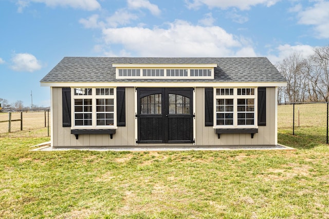 exterior space with a shingled roof, an outbuilding, and a yard