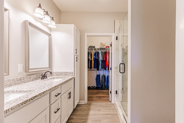 bathroom with double vanity, a spacious closet, a stall shower, a sink, and wood finished floors