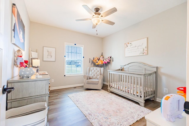 bedroom featuring a crib, wood finished floors, a ceiling fan, and baseboards