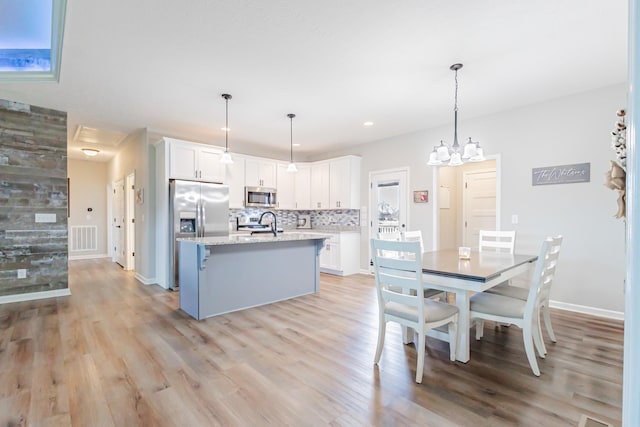 kitchen with a kitchen island with sink, stainless steel appliances, white cabinets, light wood-type flooring, and tasteful backsplash