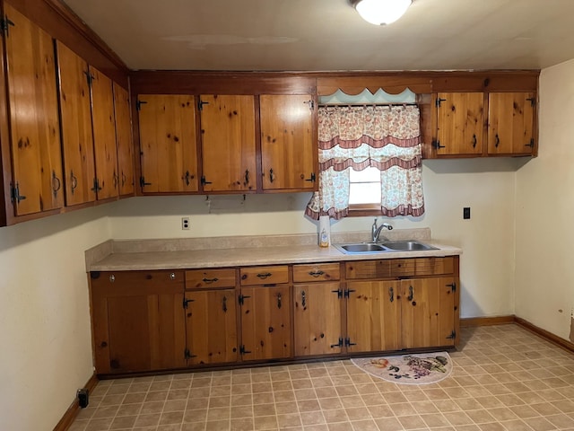 kitchen with baseboards, light countertops, a sink, and brown cabinets