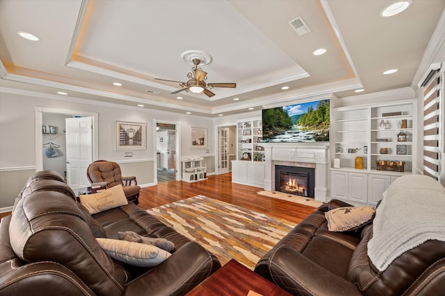 living area with a fireplace with flush hearth, wood finished floors, visible vents, ornamental molding, and a tray ceiling