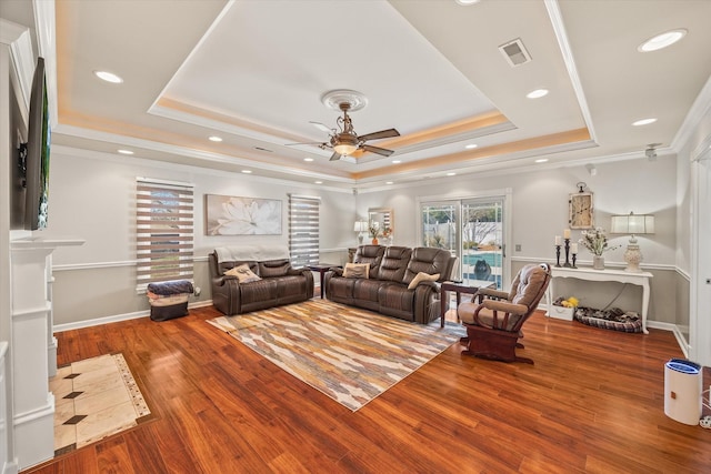 living area featuring baseboards, visible vents, ornamental molding, wood finished floors, and a tray ceiling