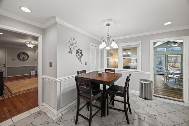 dining room with ornamental molding, ceiling fan with notable chandelier, wainscoting, and light tile patterned floors