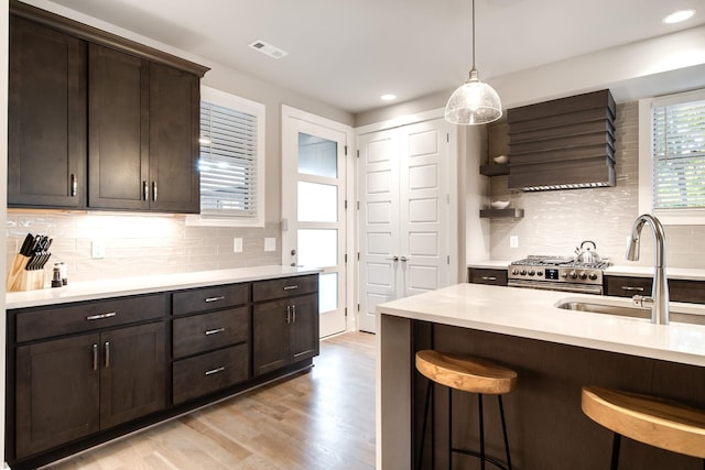 kitchen with a breakfast bar area, dark brown cabinetry, a sink, light countertops, and wall chimney range hood