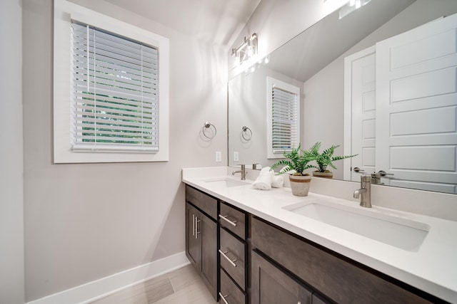 bathroom featuring lofted ceiling, a sink, baseboards, and double vanity