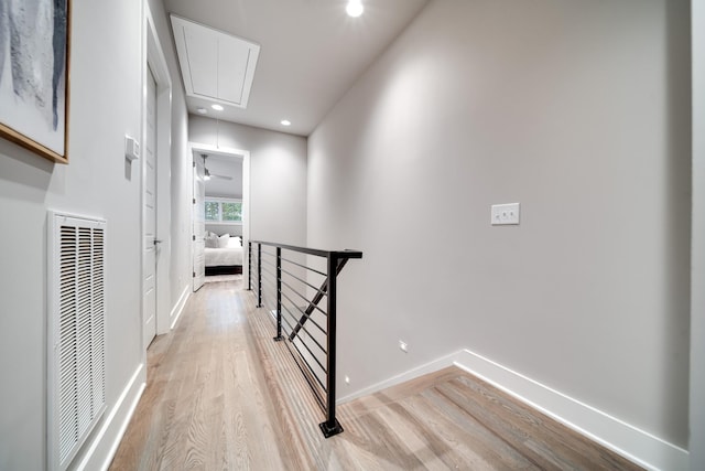 hallway with light wood finished floors, attic access, visible vents, baseboards, and an upstairs landing