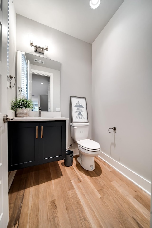 bathroom with toilet, wood finished floors, visible vents, vanity, and baseboards