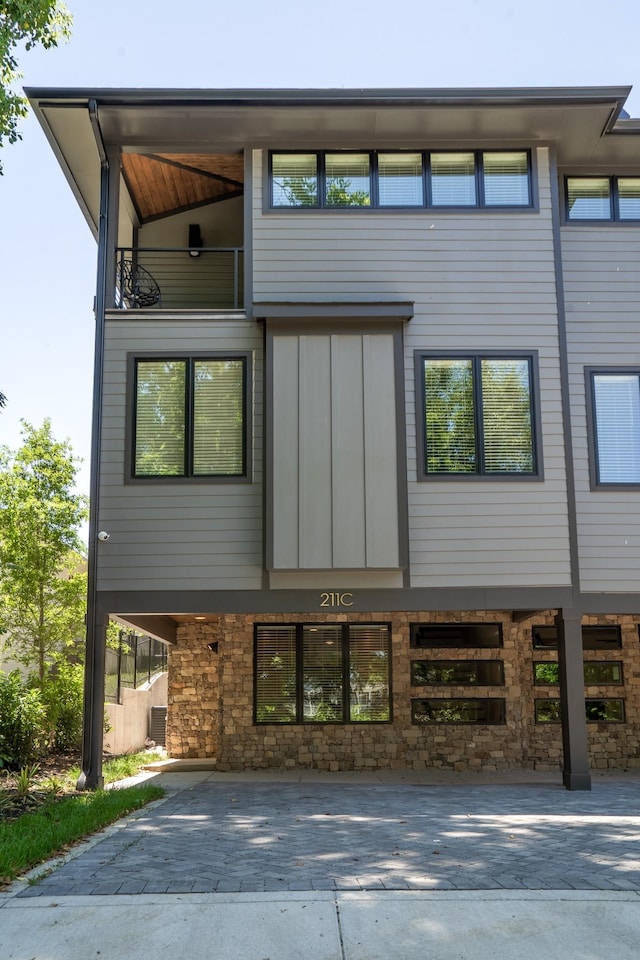 exterior space with a balcony, stone siding, and decorative driveway