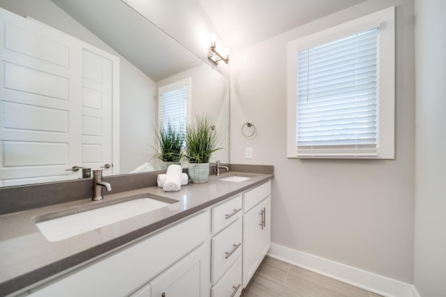 bathroom featuring vaulted ceiling, double vanity, a sink, and baseboards