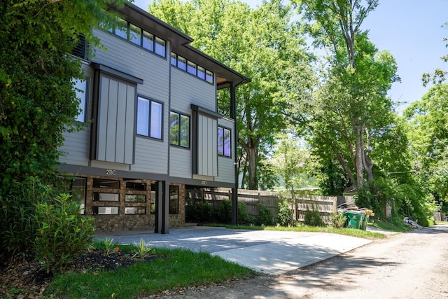 view of property exterior with board and batten siding, concrete driveway, and fence