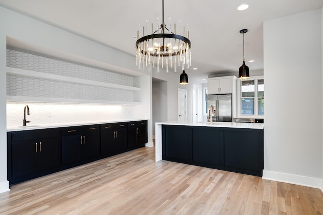 kitchen with stainless steel refrigerator with ice dispenser, open shelves, light countertops, a sink, and dark cabinets