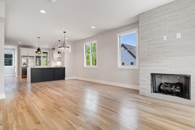 unfurnished living room with baseboards, a tile fireplace, light wood-type flooring, a sink, and recessed lighting