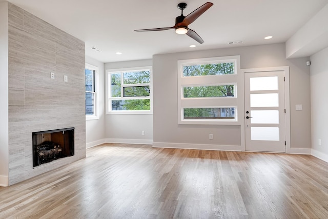 unfurnished living room with light wood-type flooring, a tile fireplace, visible vents, and baseboards