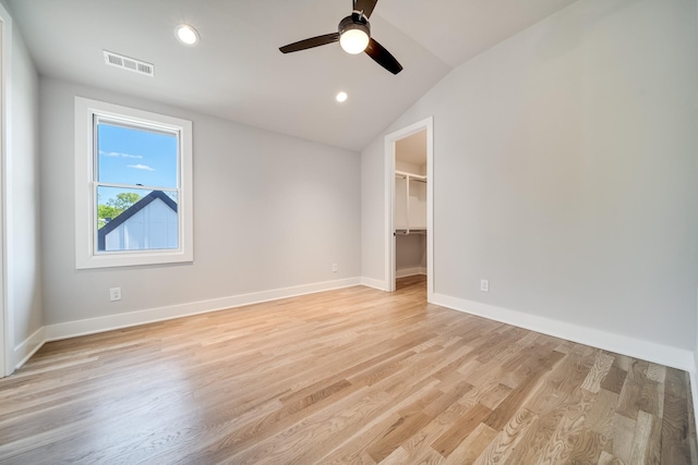 unfurnished bedroom featuring visible vents, baseboards, vaulted ceiling, a spacious closet, and light wood finished floors