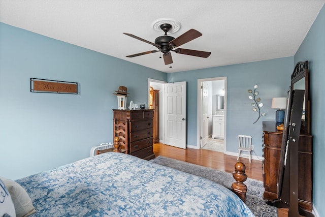 bedroom featuring a ceiling fan, ensuite bath, baseboards, and wood finished floors