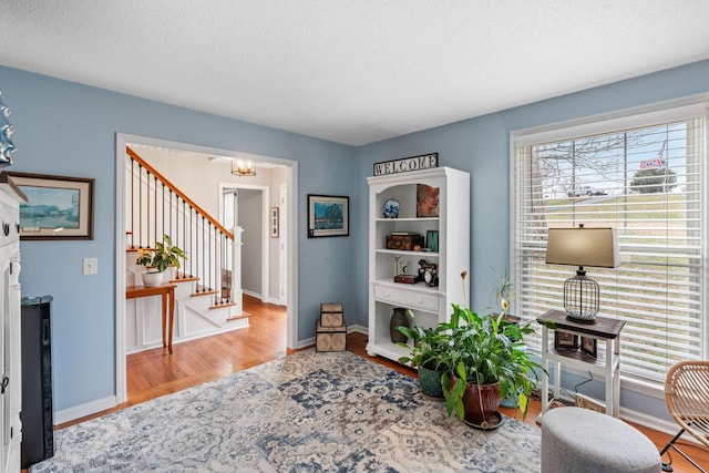 sitting room featuring a textured ceiling, stairs, baseboards, and wood finished floors