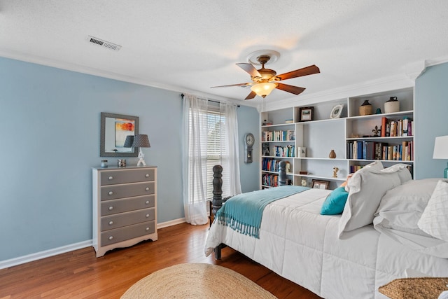 bedroom featuring a textured ceiling, wood finished floors, visible vents, and crown molding